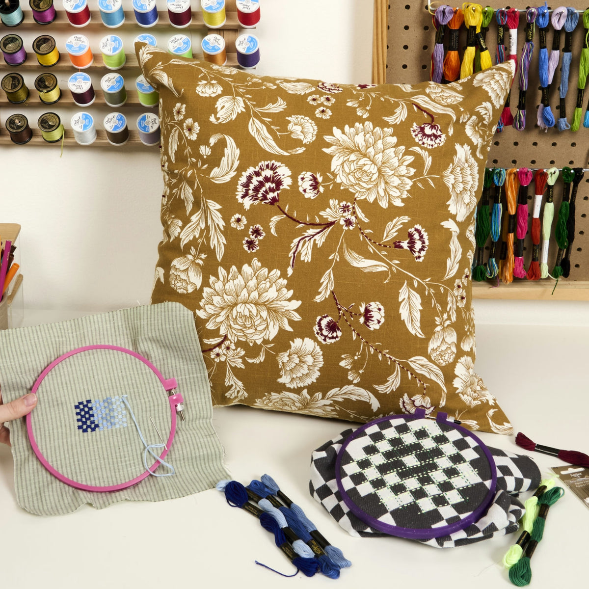Floral-patterned pillow with embroidery hoops and thread spools in a craft setting, a banner of a blog.