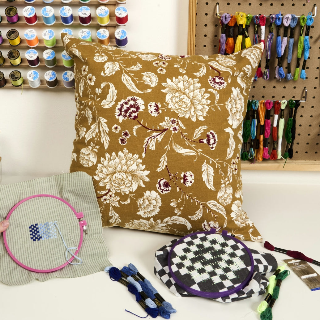 Floral-patterned pillow with embroidery hoops and thread spools in a craft setting, a banner of a blog.