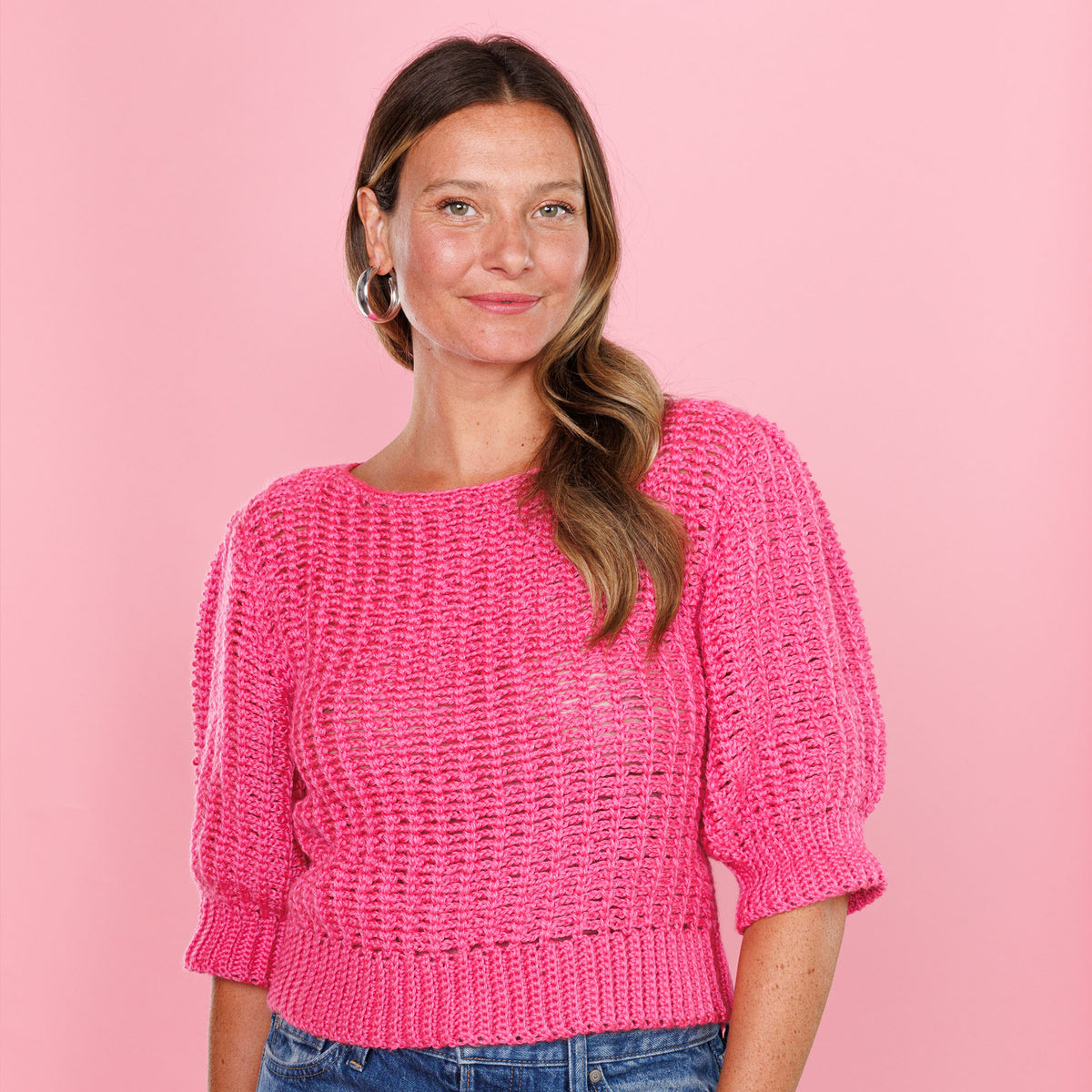 Woman wearing a pink knitted sweater against a pink background