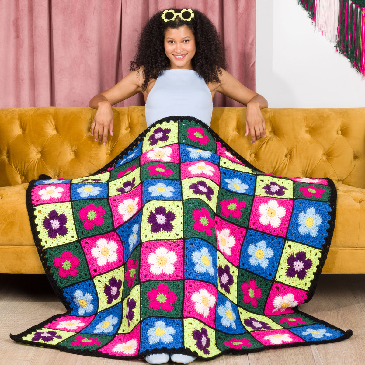 A crocheted blanket with a colorful floral pattern made using Red Heart All in One Flower Power yarn, Version 1