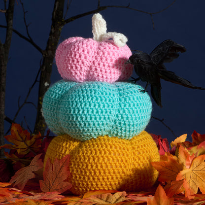 Red Heart Crochet Pumpkin Topiary Crocheted stack of pumpkins with a crow on a dark blue background with autumn leaves.